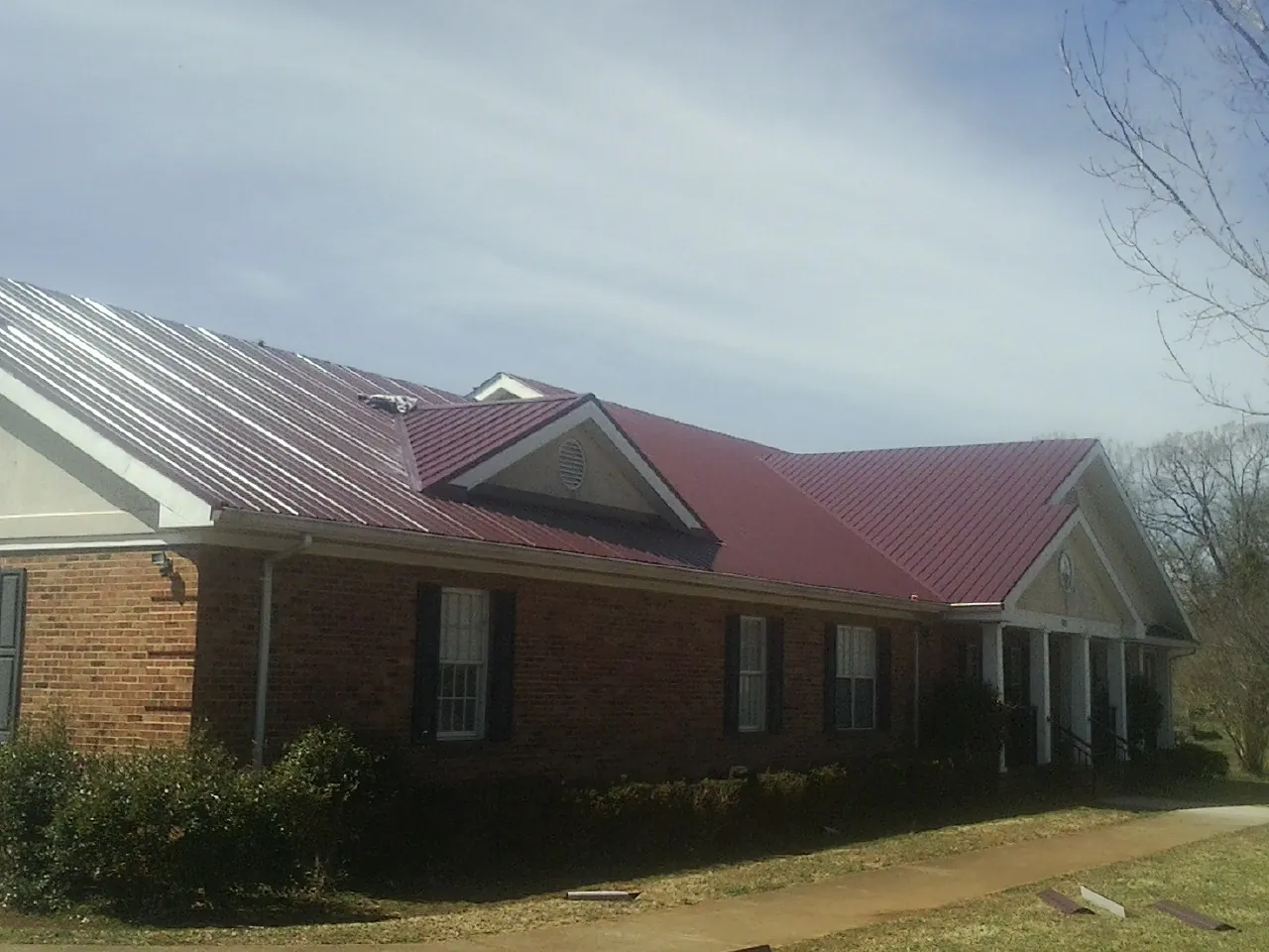 Red metal roof with gabled entries on a long brick building, from a Hail Damage Roof Repair job in Sugar Grove