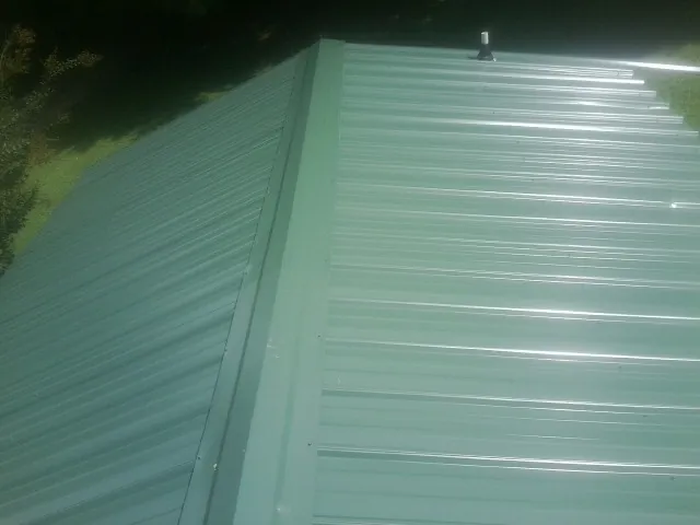 New green metal panels meeting at the ridge of a roof — Flat Roof Repair work by our crew in Sugar Grove