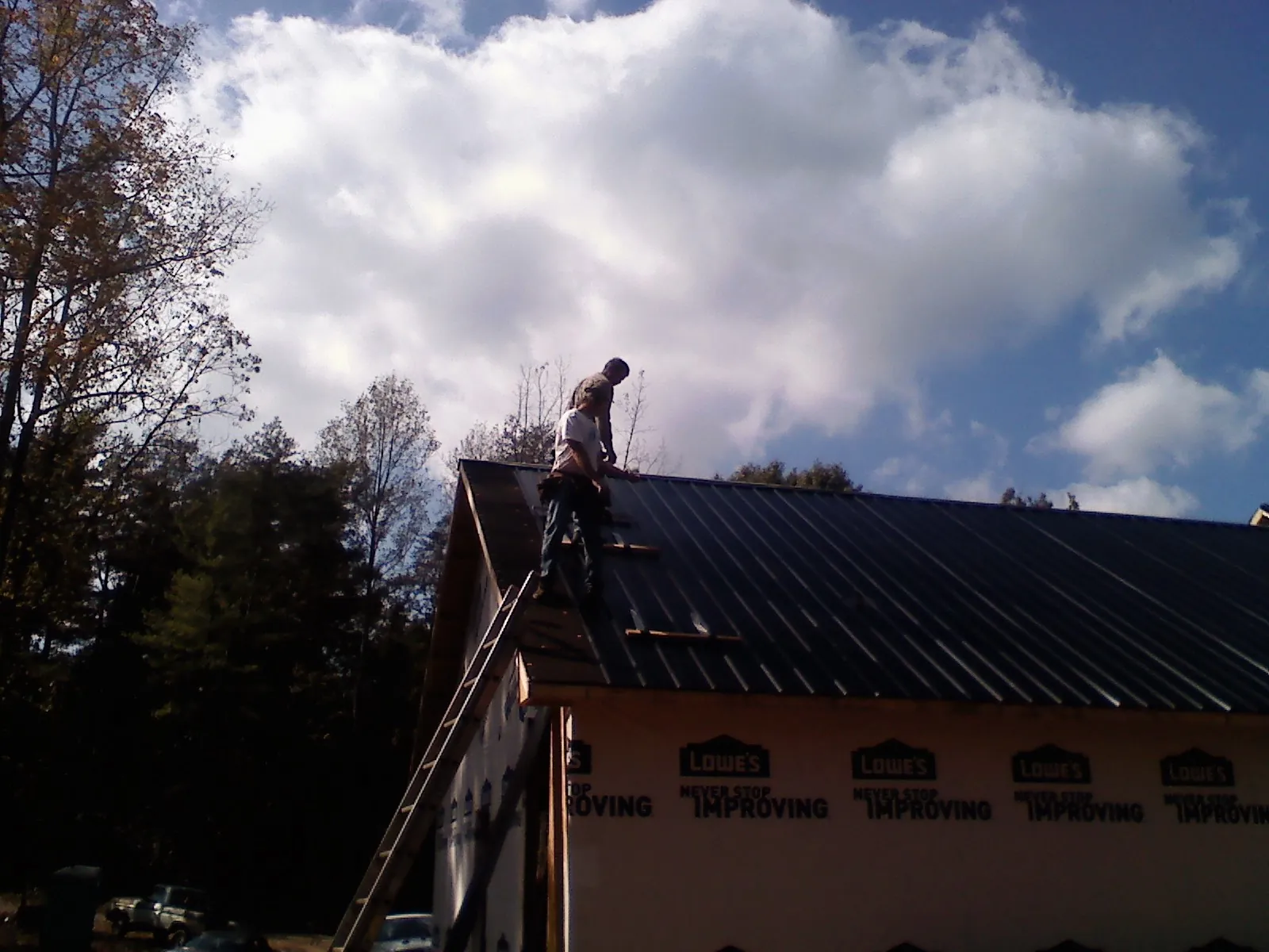 Roofer fastening dark metal panels high against a cloudy sky, from a Roof Inspection job in Sugar Grove